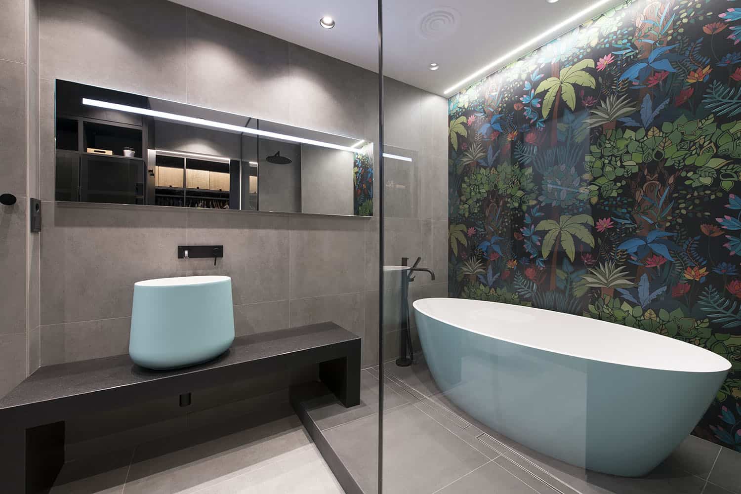 The bathroom is clad with grey tiles, a dark floral wall makes a statement and aqua appliances add to the space