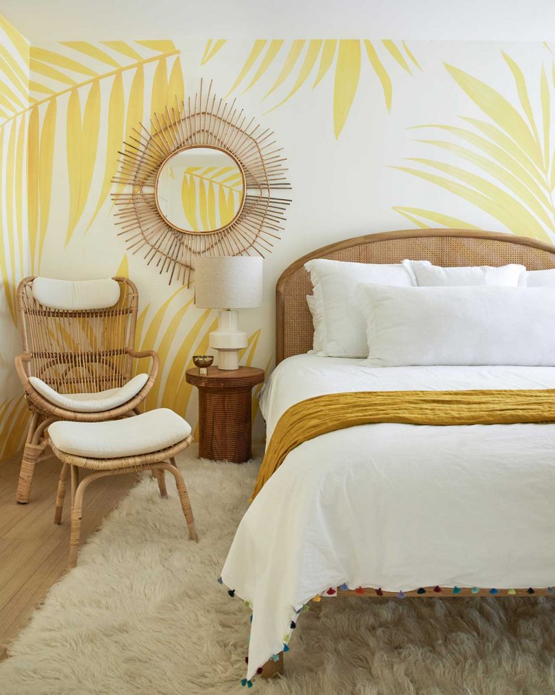 This sunny yellow bedroom shows off leaf printed wallpaper and a rattan mirror and chair
