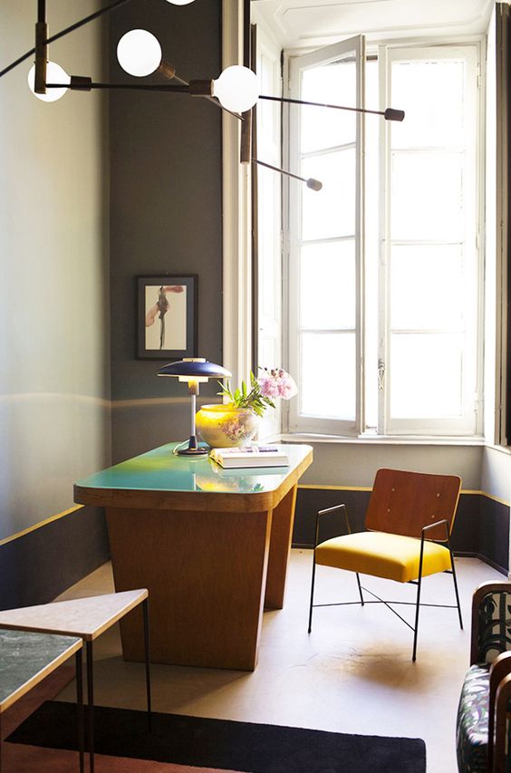 a bold home office with a grey walls, yellow edges, a catchy yellow desk with a green countertop, a yellow chair, a table lamp and some pendant ones