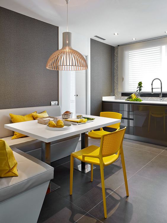 a bold modern dining nook in the kitchen, with a corner seat, a table, bright yellow chairs and a pretty lamp