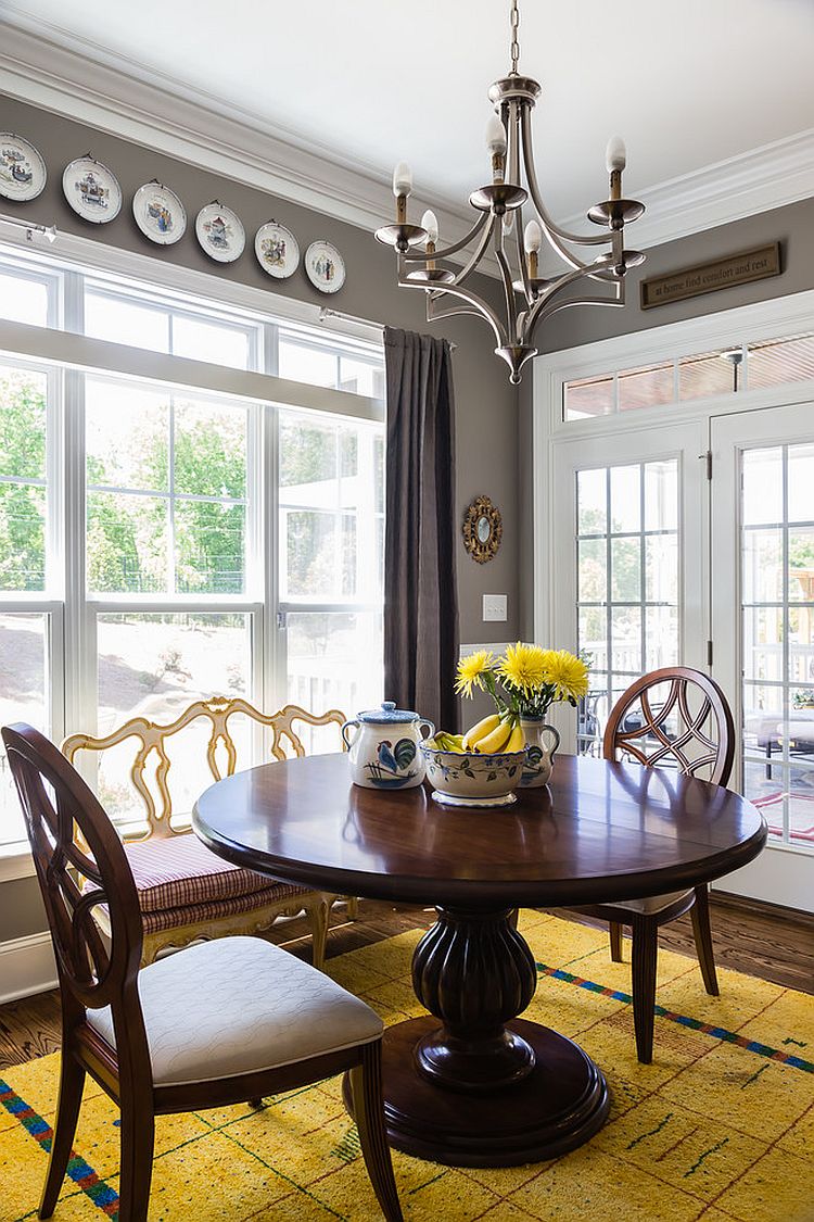 a bold vintage dining room with grey walls, a large window, a heavy round table and chairs, decorative plates and a bold yellow rug