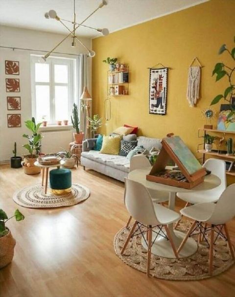a bright boho living room with a yellow accent wall, neutral furniture, books, potted plants, touches of greenery and a jute rug