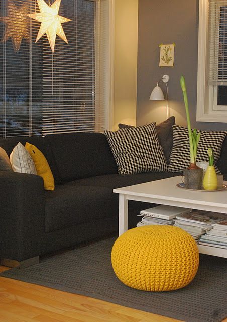 a bright living room with a black sectional, grey walls and a grey rug, sunny yellow accessories and lamps and lights