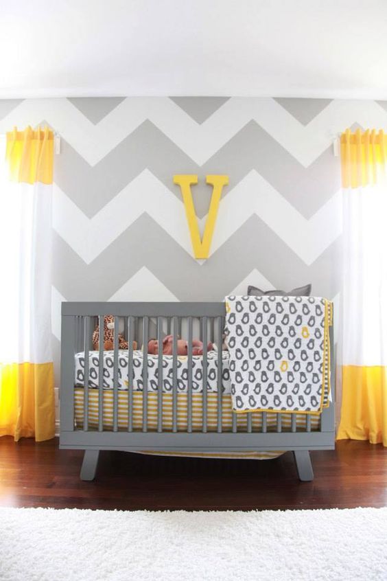a bright nursery with grye and white chevron walls, color block curtains, a grey crib and printed bedding plus a monogram on the wall