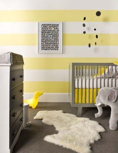 a bright nursery with striped yellow and white walls, grey furniture, a faux fur rug, a mobile and a toy elephant