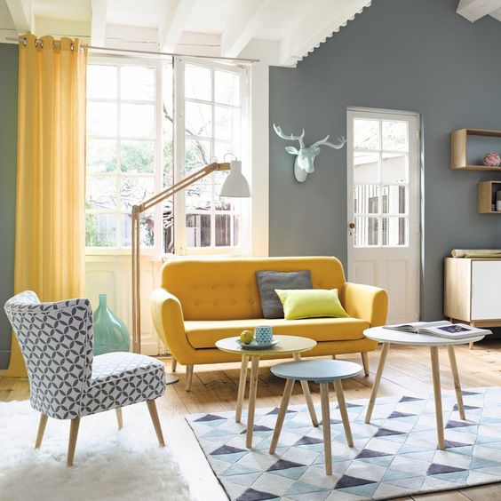 a chic living room with grey walls, a yellow sofa and a printed chair, yellow curtains and round coffee tables