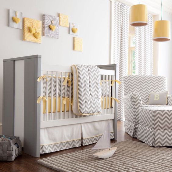 a chic neutral nursery with a grey and white crib, a grey chevron chair with an ottoman, chevron bedding, a grey and yellow gallery wall and yellow pendant lamps