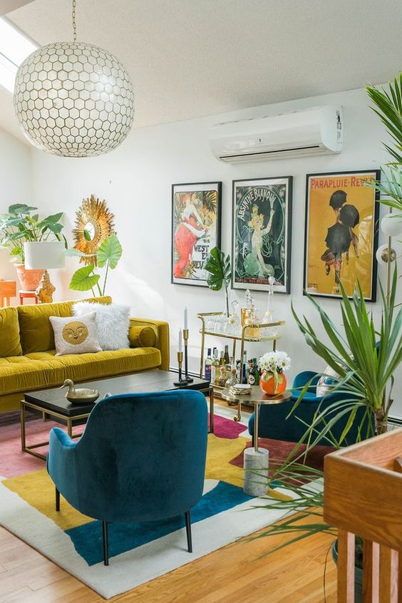 A colorful mid century modern living room with a mustard sofa, a bold rug, teal chairs, a bright gallery wall and potted plants