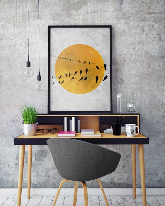 a contemporary home office with grey concrete walls, a pretty black and yellow desk, a grey chair, pendant lamps and a bold print