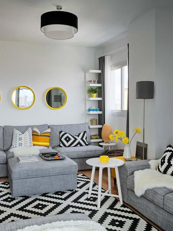 a contemporary living room with grey furniture, white shelves and a table, some lemon yellow accents here and there