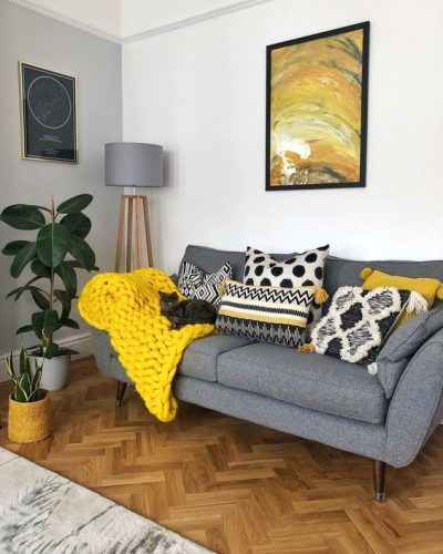 a cozy living room with a grey sofa, a grey floor lamp, a lemon yellow blanket and pillows plus a bold artwork