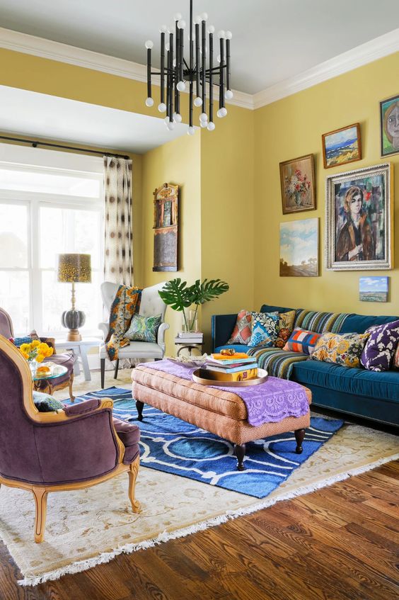 a crazily colorful living room with yellow walls, a navy sofa, a pink ottoman and a purple chair, colorful rugs, pillows and upholstery
