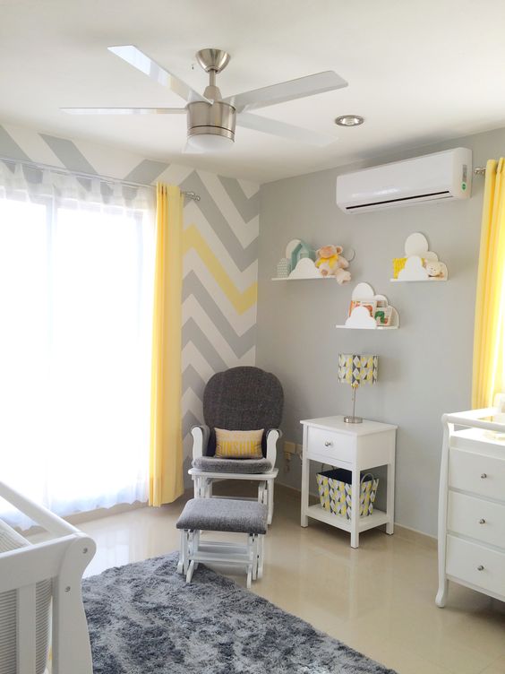 A grey nursery with a chevron, white furniture, a grey chair with a stool and cloud shaped shelves for books