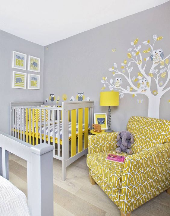 a grey nursery with a tree with owls, a grey and yellow crib, a mustard printed chair and a pretty gallery wall