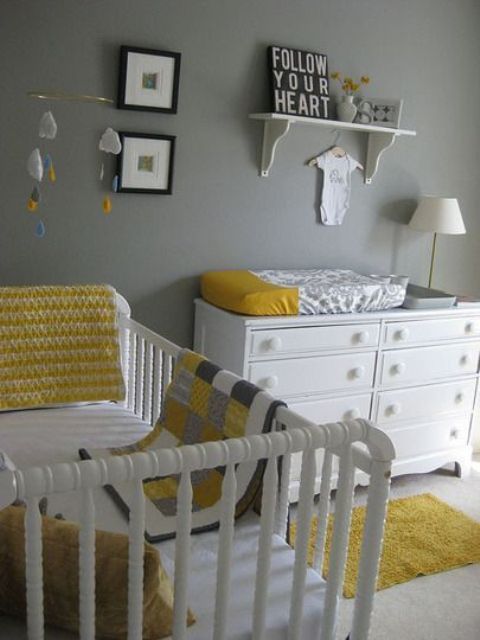A grey nursery with white furniture, touches of yellow   some linens, a gallery wall and a shelf with some art is very cute