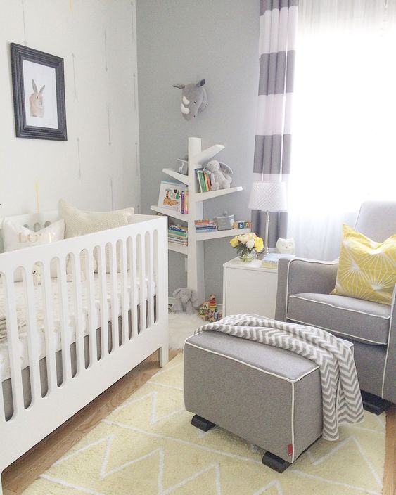 a grey, white and yellow nursery with grey walls, color block curtains, a grey chair and an ottoman, a white crib and yellow touches