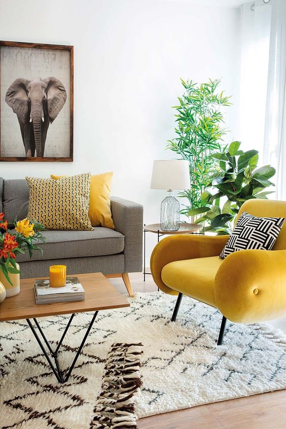 A mid century modern living room with a grey sofa, a lemon yellow chair, printed pillows, potted plants and a bold artwork