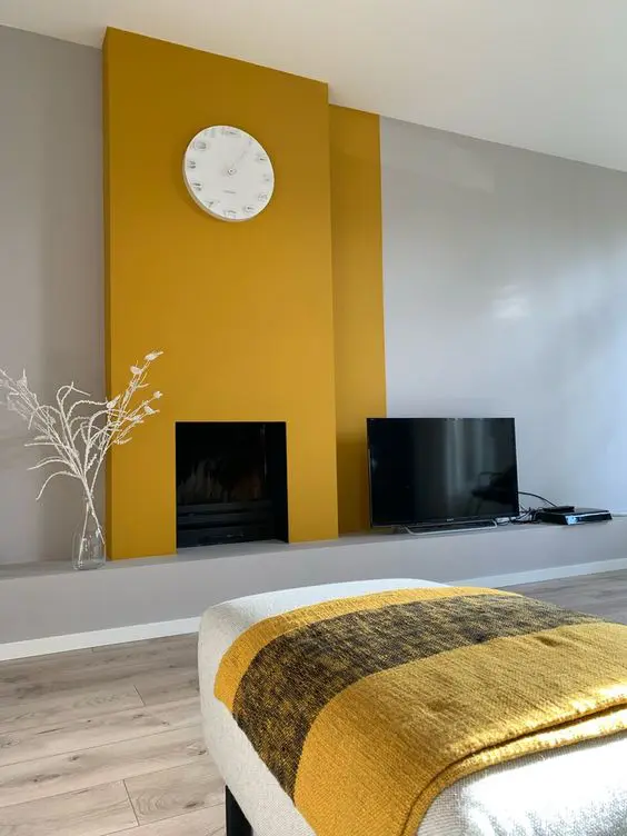 a minimalist living room with dove grey walls, mustard panels over the fireplace, a clock and a daybed with a yellow blanket