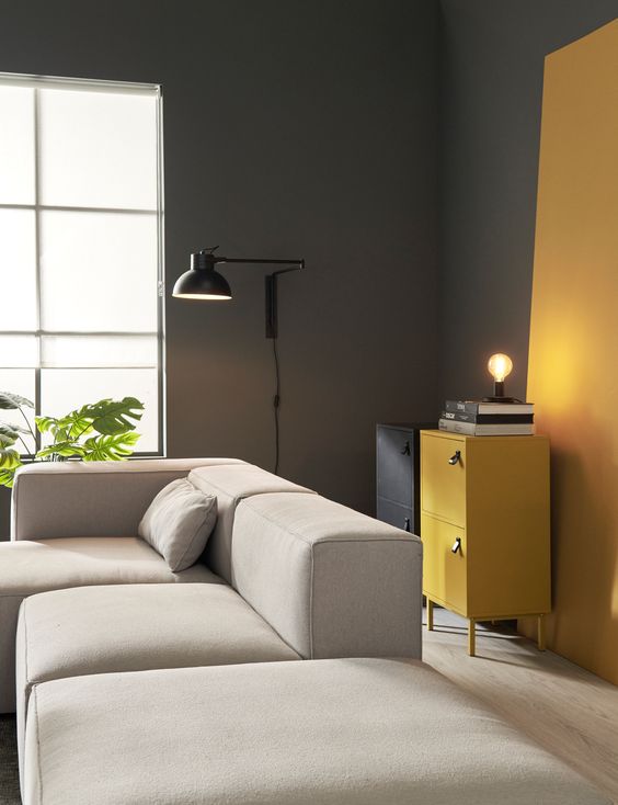 a minimalist living room with grey walls, honey yellow touches, a black and a honey yellow cabinet, a creamy sectional and a black lamp