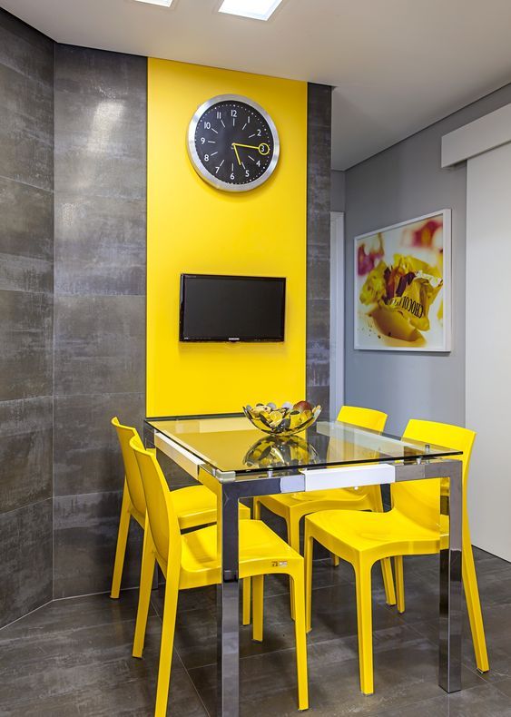 a modern colorful dining room with a glass dining table, yellow chairs, a grey wall with a color block effect done with a yellow panel