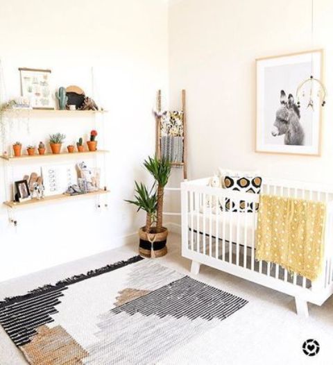 a neutral boho nursery with neutral furniture, a boho rug, a suspended shelf, mustard bedding and a wall art