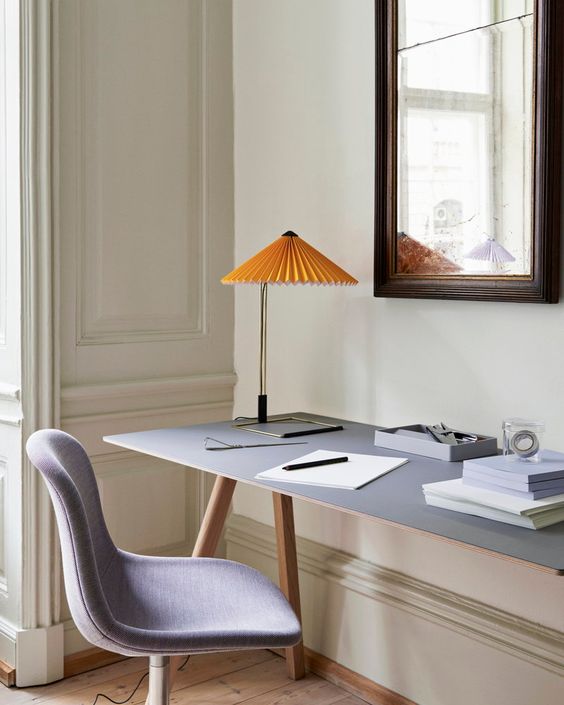 a neutral sophisticated home office with a grey trestle desk, a grey chair and a yellow lamp with a pleated shade