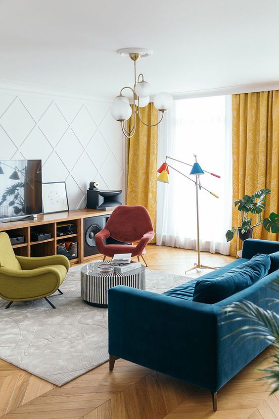 a pretty mid-century modern living room with a navy sofa, red and lemon chairs, yellow curtains, colorful lamps