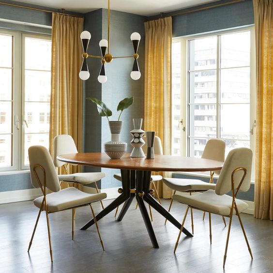 a refined and elegant grey and yellow dining room with grey walls, yellow curtains, a round dining table, neutral chairs and a pretty chandelier
