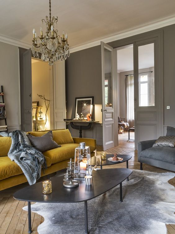 a refined dove grey living room with a mustard sofa, grey chairs, cool coffee tables and a crystal chandelier plus artworks