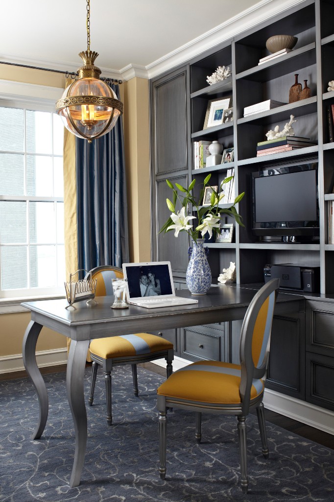 a refined home office with yellow walls, a large built in grey storage unit, a grey desk and grey and yellow chairs, grey curtains and a chic pendant lamp