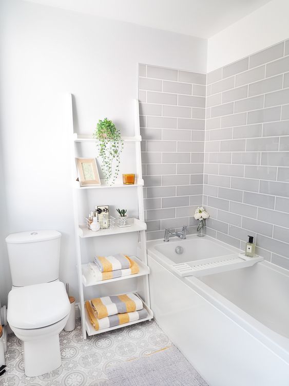 a serene bathroom with grey subway tiles, white appliances and a shelf, grey, white and yellow towels