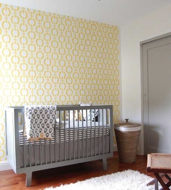 a simple and cute nursery with a yellow accent wall, a grey crib, printed bedding and woven touches