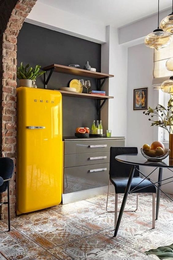 a sleek grey kitchen with a chalkboard wall, open shelves, a sunny yellow fridge and a dining zone with pendant lamps