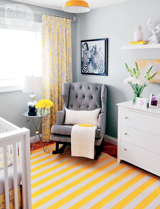 a small and cozy grey nursery with a striped rug, white furniture, a grey rocker, bold yellow textiles and a pendant lamp