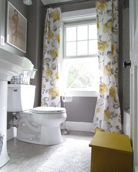 a small vintage bathroom with grey walls and a floor, grey and yellow floral curtains, white appliances is a very chic space