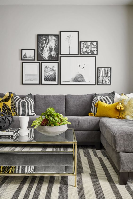 a stylish living room with a grey corner sofa, a striped rug, a tiered coffee table, a black and white gallery wall and some yellow pillows