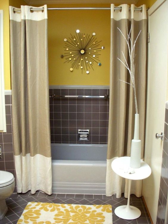 A stylish mid century modern bathroom with yellow and grey walls, a sunburst decoration, color block curtains