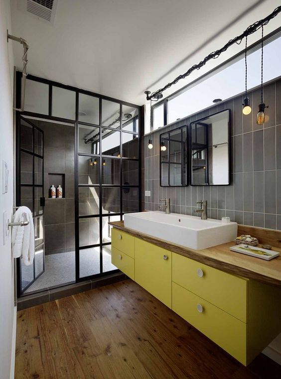 a super chic bathroom with grey tiles, a floating yellow vanity, a wooden countertop, a shower space with a framed glass space divider