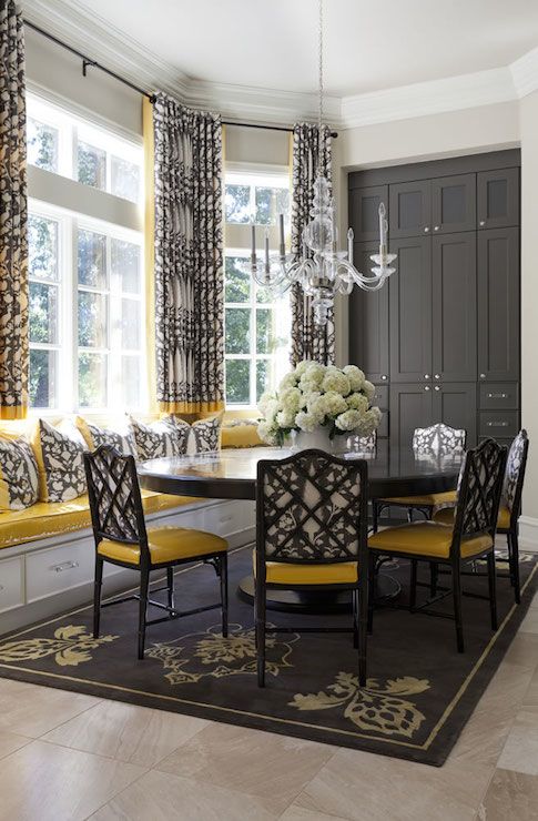 a vintage and refined dining room with a bay window, a windowsill seat, a round table, black and yellow chairs, a graphite grey storage unit
