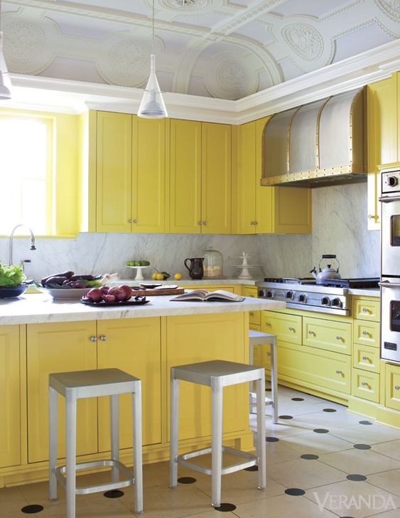 a vintage yellow kitchen with a grey marble backsplash and countertops, metal stools, a vintage metal hood