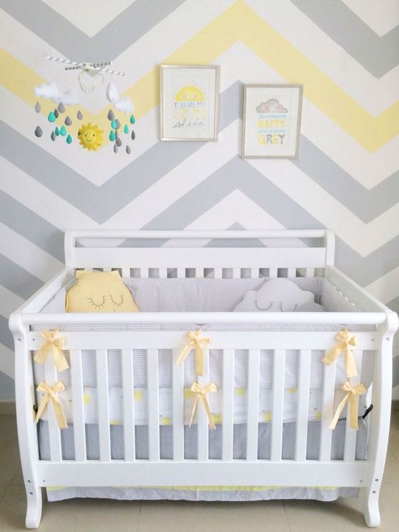 a welcoming nursery with a chevron accent wall, a white crib with grey and yellow bedding, a bright mobile and artworks