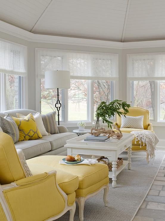 a welcoming vintage living room with yellow and neutral furniture, printed pillows, greenery, a floor lamp and a bay window
