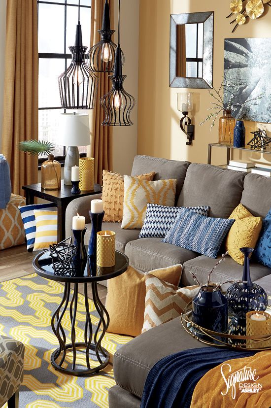 a whimsical living room with yellow walls, grye furniture, blue and yellow pillows and blankets, pendant lamps and a coffee table plus touches of navy