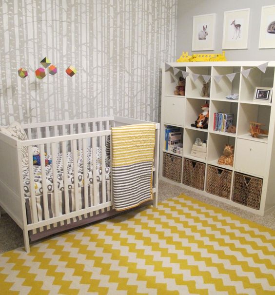 a woodland nursery with woodeland wallpaper, white furniture, a bright chevron rug, printed bedding and a cute gallery wall