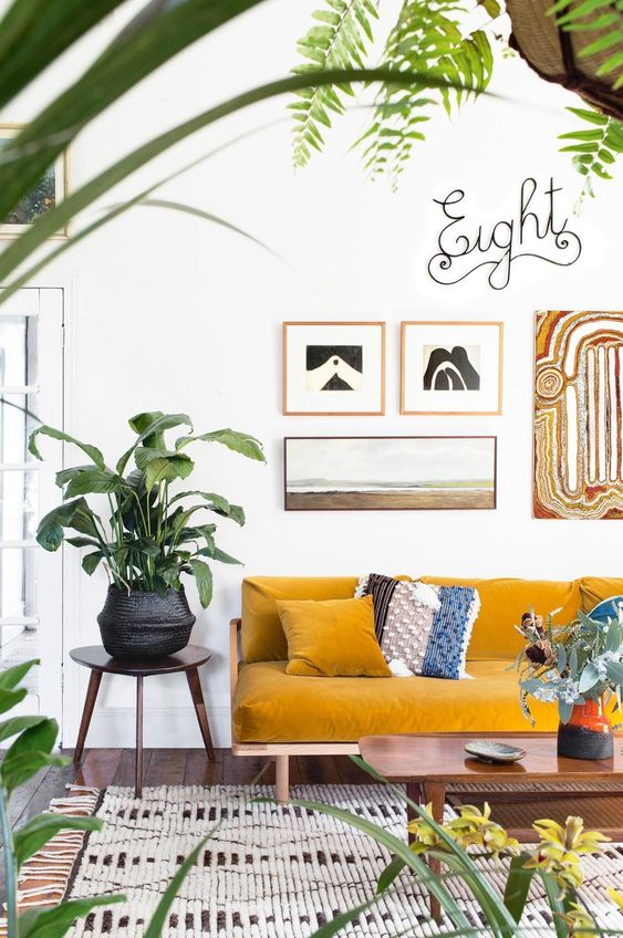 an airy boho living room with a mustard sofa, printed textiles and a gallery wall, potted blooms and greenery and calligraphy