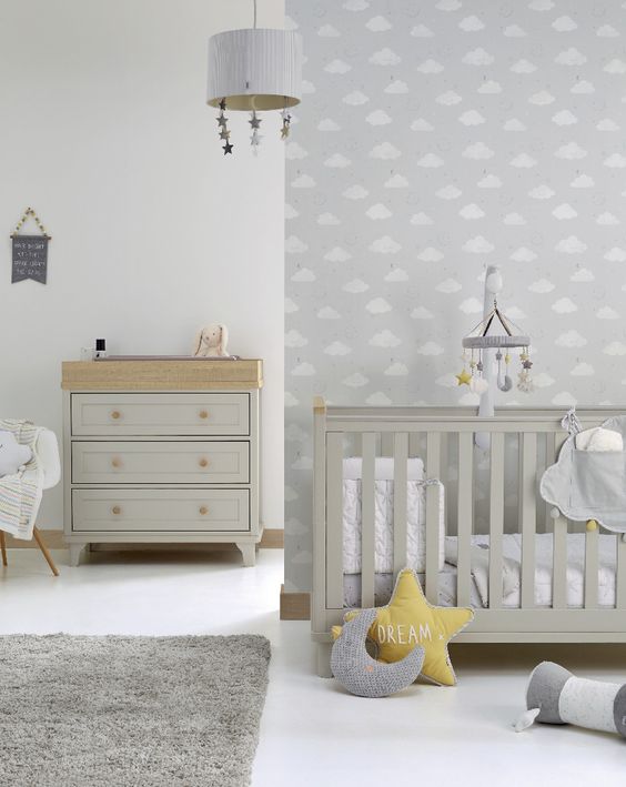 an airy grey and white nursery with a grey crib and dresser, mustard and grey pillows, mobiles and a cozy rug