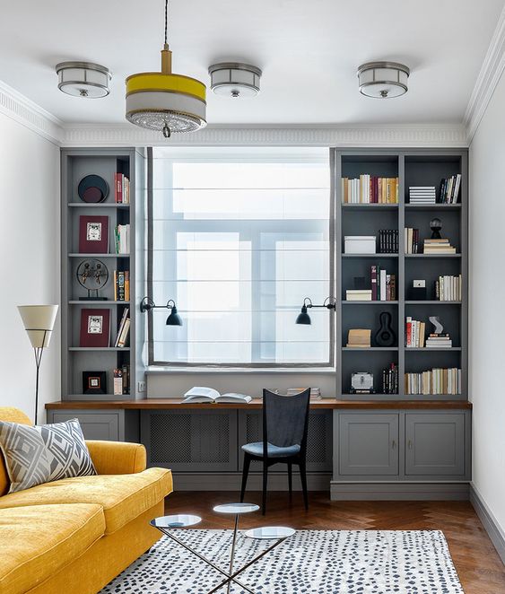 an elegant vintage home office with a built-in grey storage unit, a vintage chair, a yellow sofa, a coffee table trio and a pendant lamp