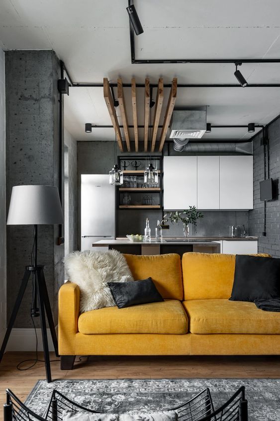an industrial grey space with white cabinetry, black exposed pipes and a bold accent – a honey yellow sofa that makes a statement