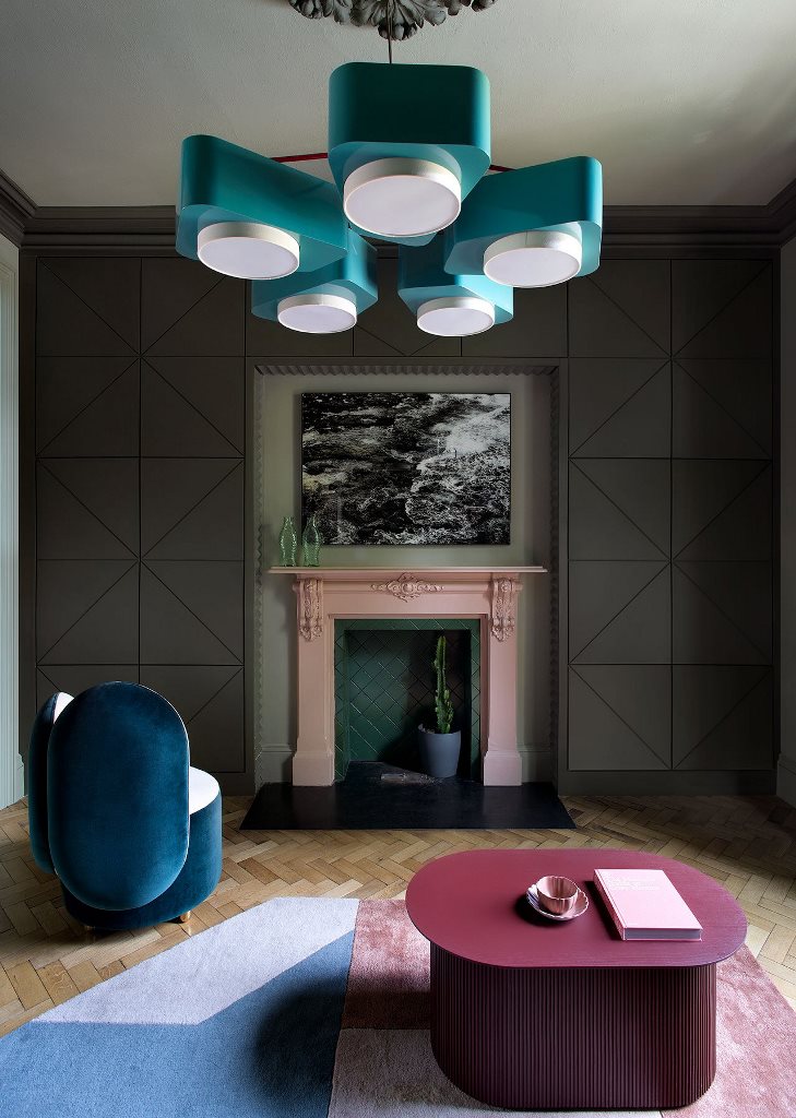 The living room features a green and pink fireplace, a blue chandelier, a navy chair and a burgundy table