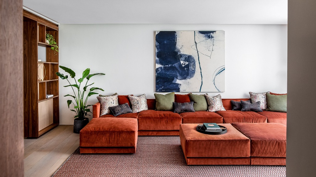 The living room shows off a fantastic rust-colored sectional, a storage unit, a blue artwork and some muted pillows